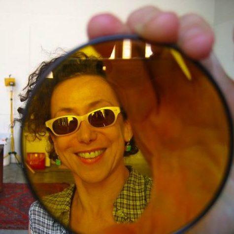 Abigail Child author photo, holding a circular yellow tinted lens in front of her face