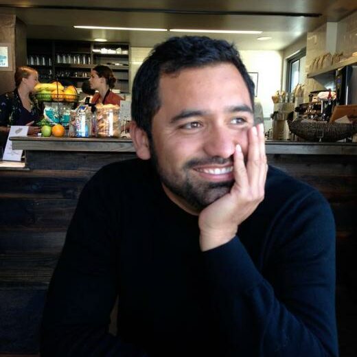 Hugo Garcia Manriquez author photo, inside a cafe, smiling with his chin resting in his hand
