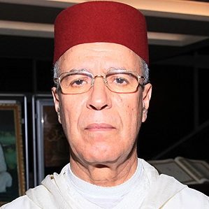 Ahmed Toufic author photo, indoors with framed iamges and an open book visible in the background