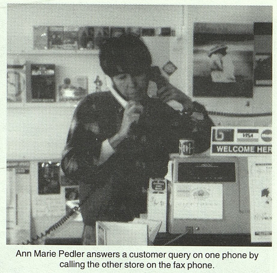 photograph of Ann Marie Pedler answering a customer query on one phone while calling another store on a fax phone