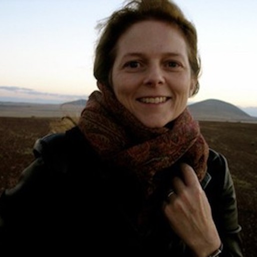 Light-skinned woman with red hair red scarf and black leather jacket against a desert landscape